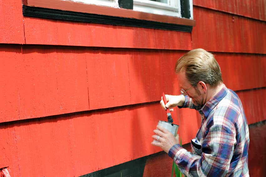 Mann streicht Haus rot